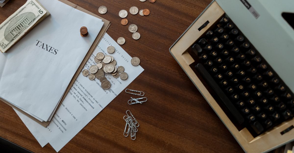 Overhead view of a vintage desk with typewriter, coins, and tax documents.