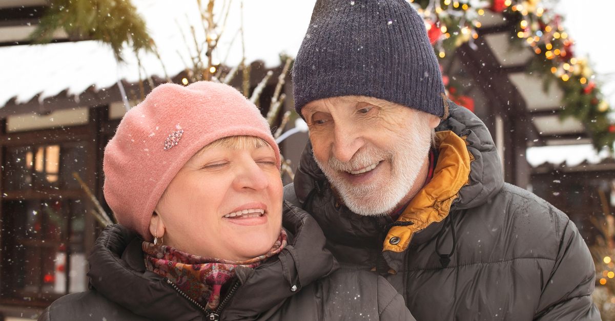 Joyful elderly couple enjoying a snowy winter day outdoors, dressed warmly in winter clothing.