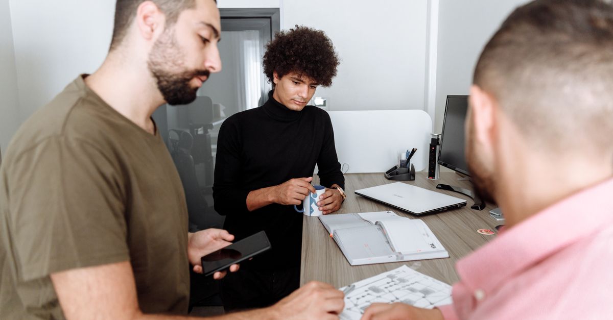 Three colleagues discussing work around a table in a modern office setting.