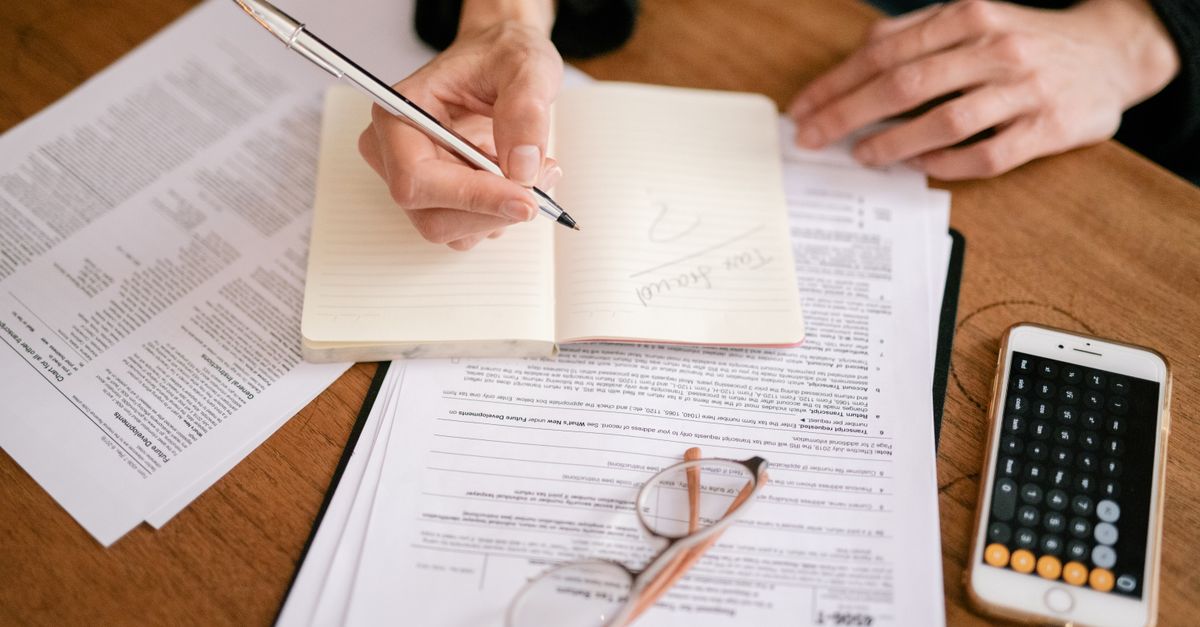 Close-up of a person writing in a notebook with documents and a calculator, managing finances.