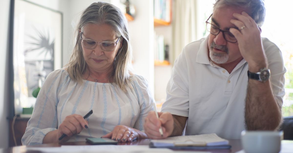 Senior couple calculating expenses at home office desk with documents and notes.