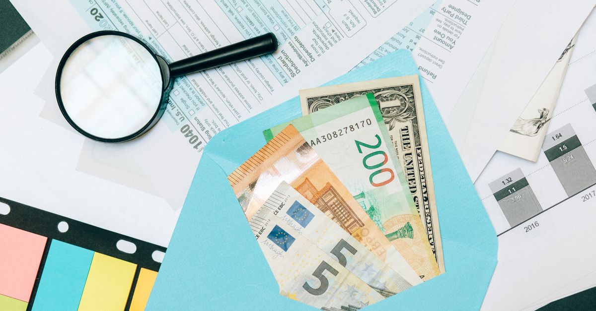 Close-up of tax documents and mixed currency in a blue envelope with a magnifying glass, perfect for financial analysis concepts.