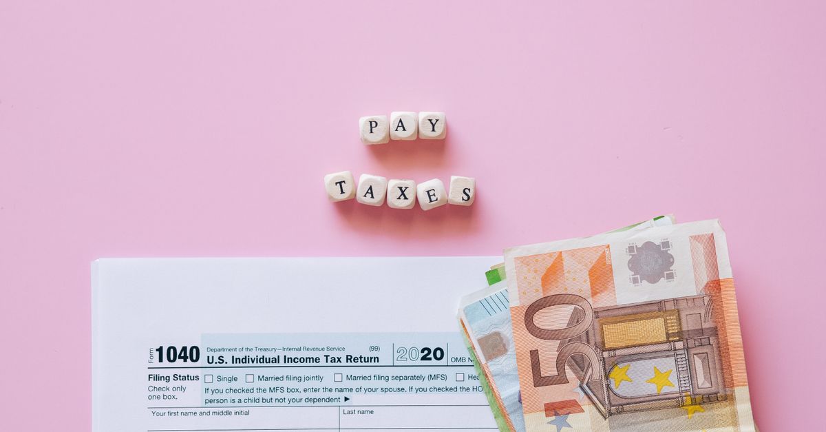 Top view of tax form, euro banknotes, and 'Pay Taxes' letter blocks on pink background.