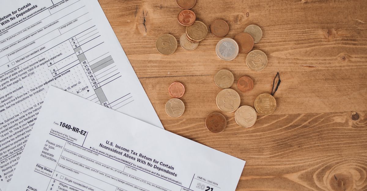 Flat lay of tax forms and scattered coins on a wooden table, illustrating finance and taxation concepts.