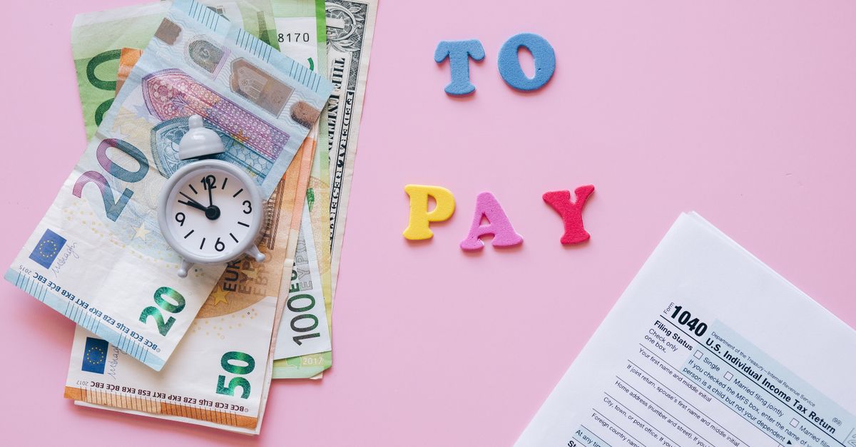 Flat lay of taxes, currency, and reminder to pay on pink background.
