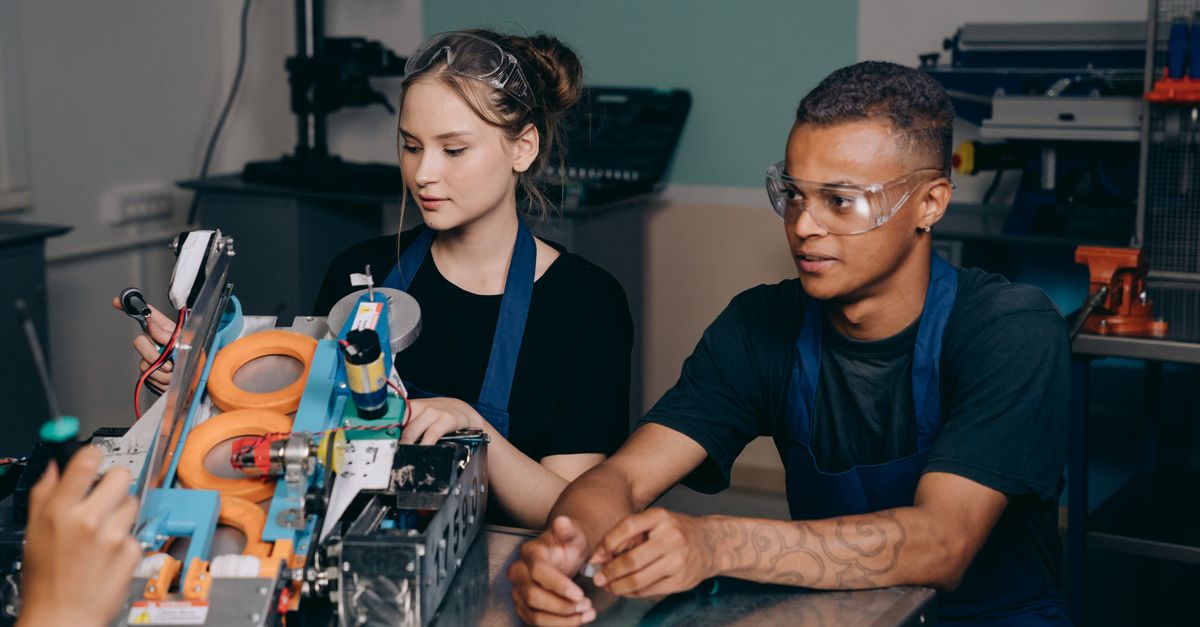 Two young engineers collaborating on a complex machine in an industrial setting.