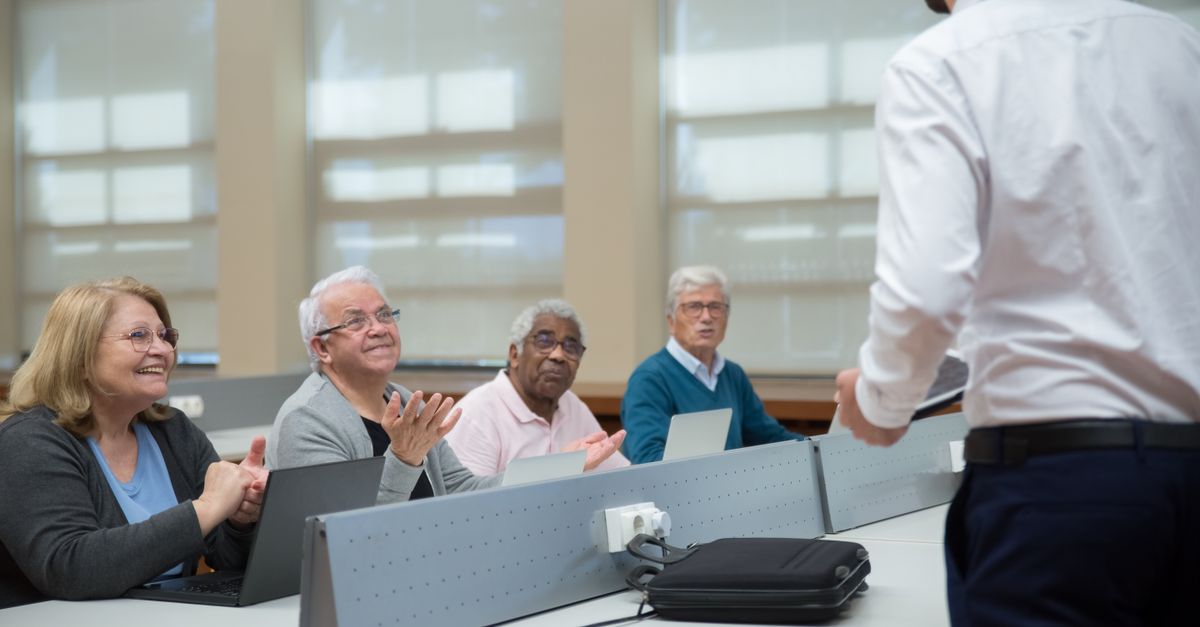 Senior adults attend a computer class, led by an instructor, in a classroom setting.