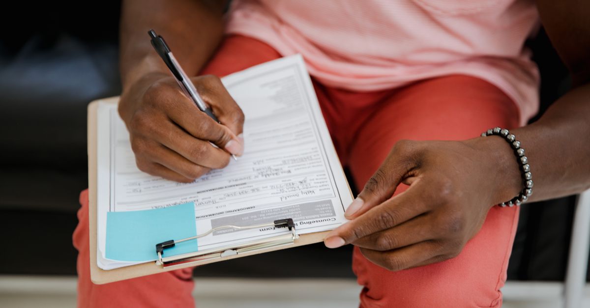 Close-up of a hand writing on a form with a pen attached to a clipboard.