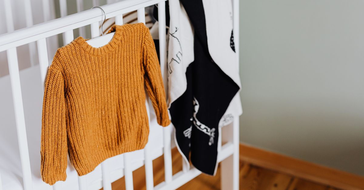 Warm mustard knitted baby sweater hanging on a white crib in an inviting nursery setting.