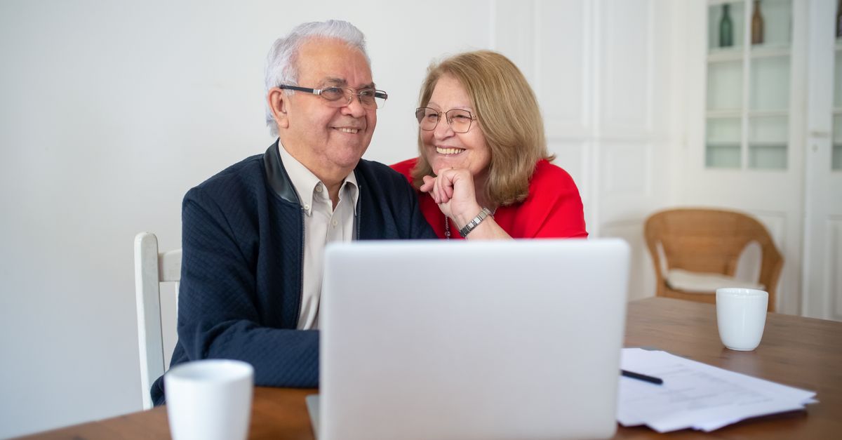 Senior couple smiling while using a laptop at home, enjoying online activities together.