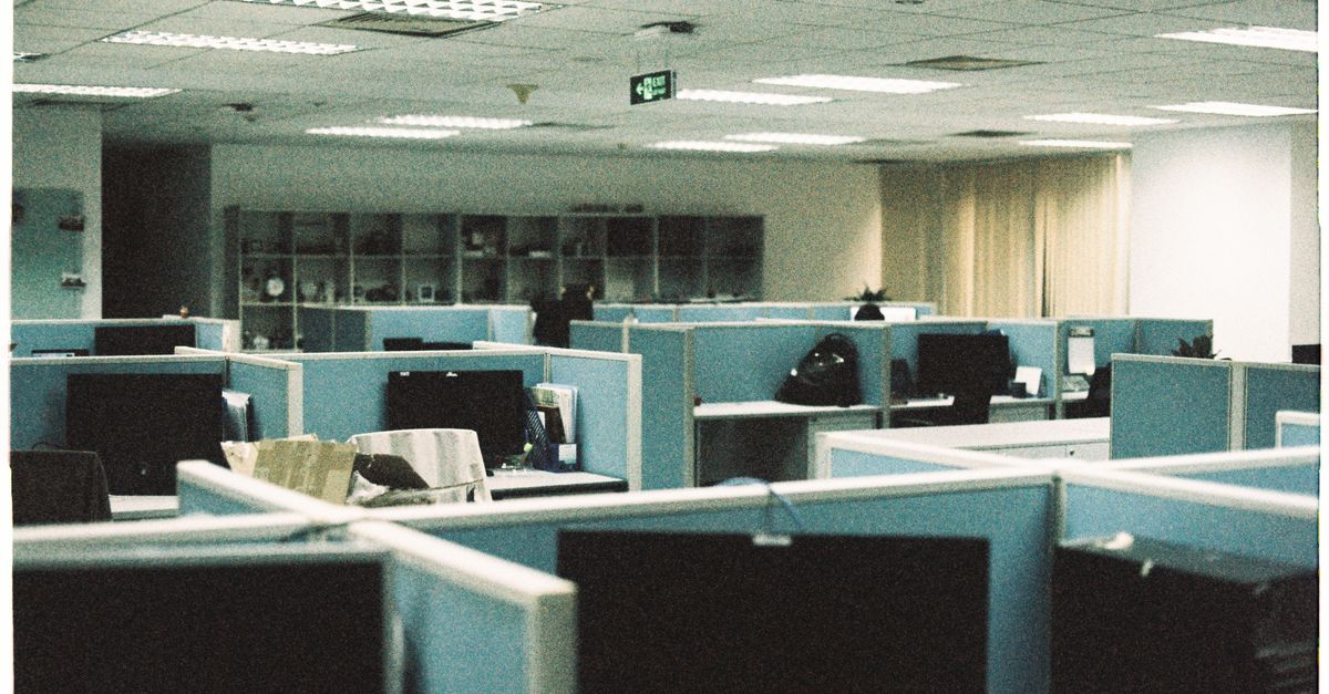 Spacious office floor with rows of empty cubicles and computer monitors.