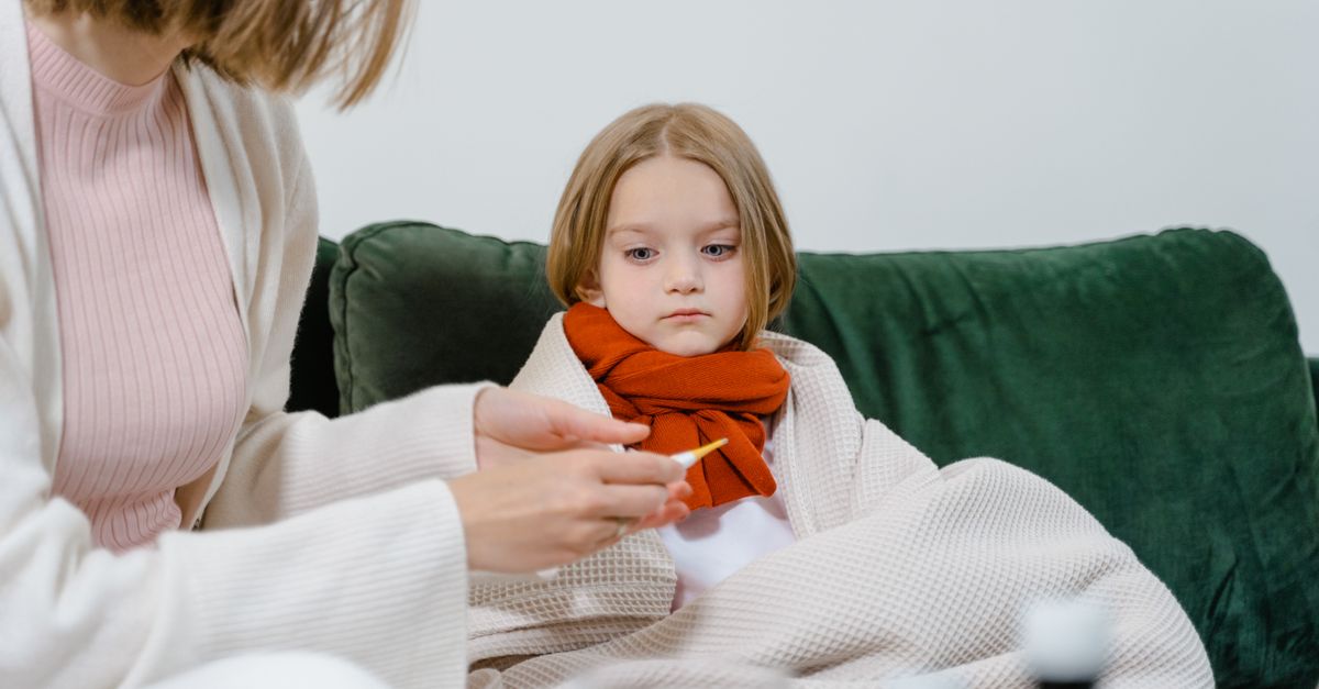 A caring moment of a woman checking a sick child's temperature on a cozy green couch indoors.