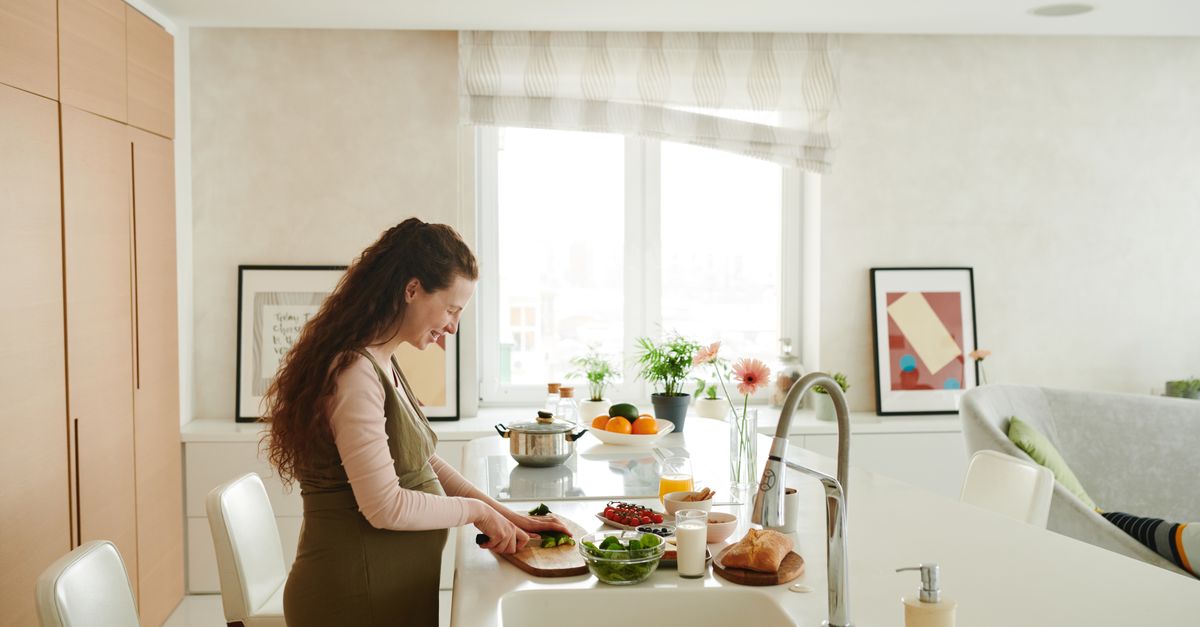 Pregnant woman slicing vegetables in a bright kitchen setting, embracing healthy lifestyle.