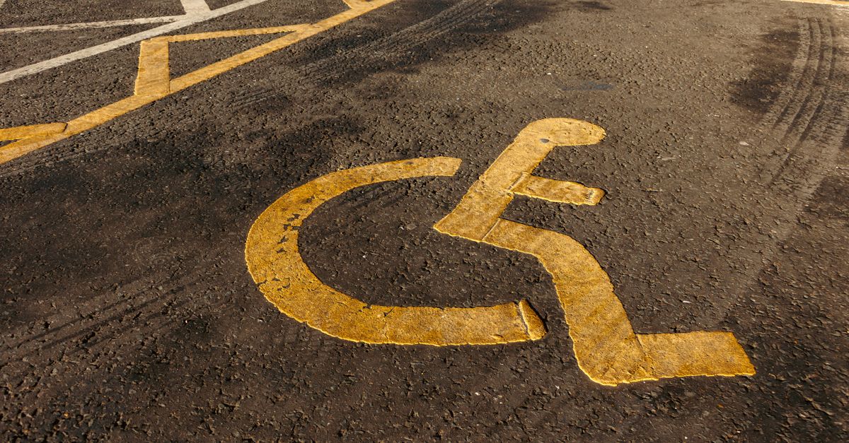 Yellow wheelchair symbol painted on asphalt in a parking lot.
