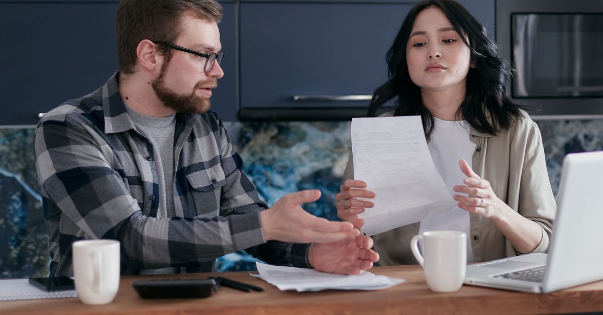 A couple having a discussion over financial documents at home with a laptop.