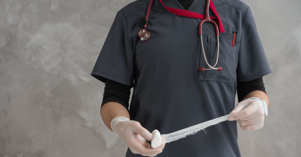 Healthcare worker preparing gauze bandage wearing stethoscope and gloves.