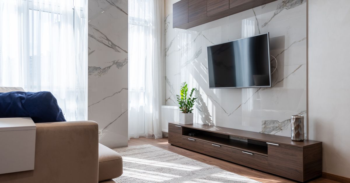 Modern TV set hanging on wall between wooden cabinets in front of comfortable sofa in light living room