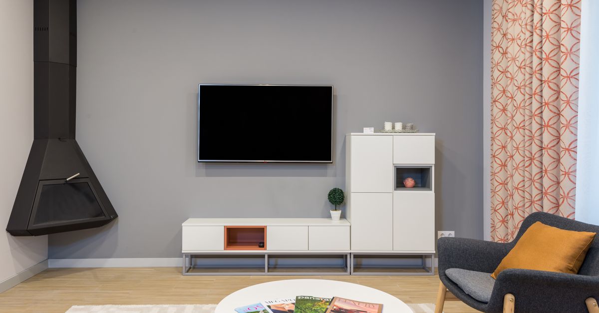 Modern TV and fireplace hanging on wall in minimalist apartment with white furniture and comfortable armchair