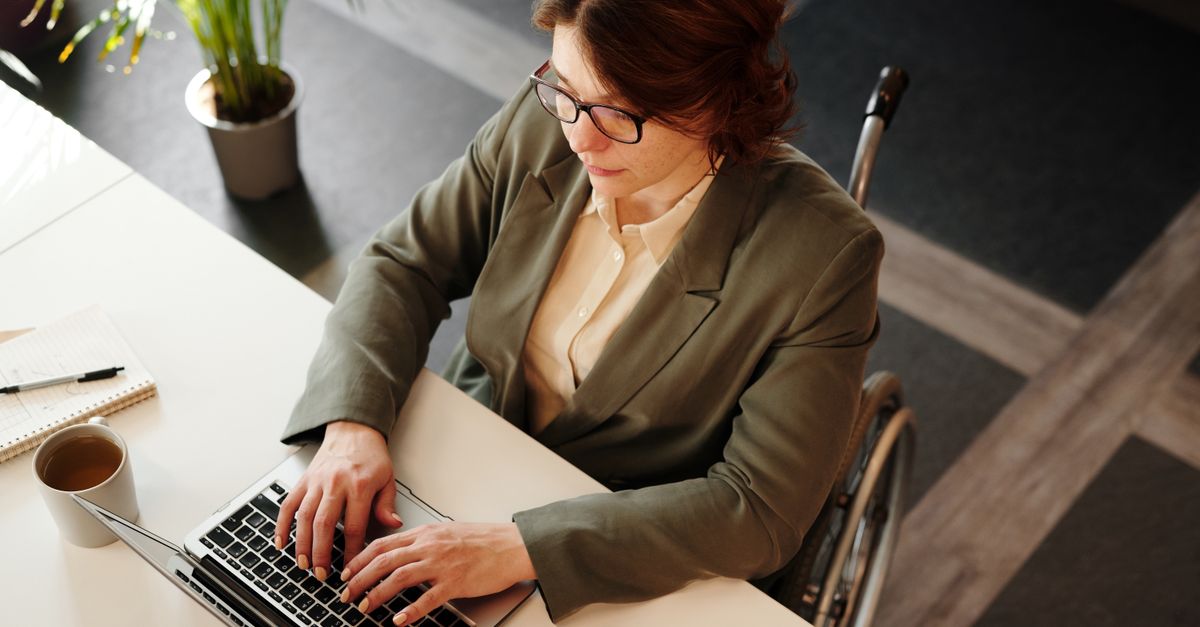 Professional woman in a wheelchair working on a laptop at an office desk.