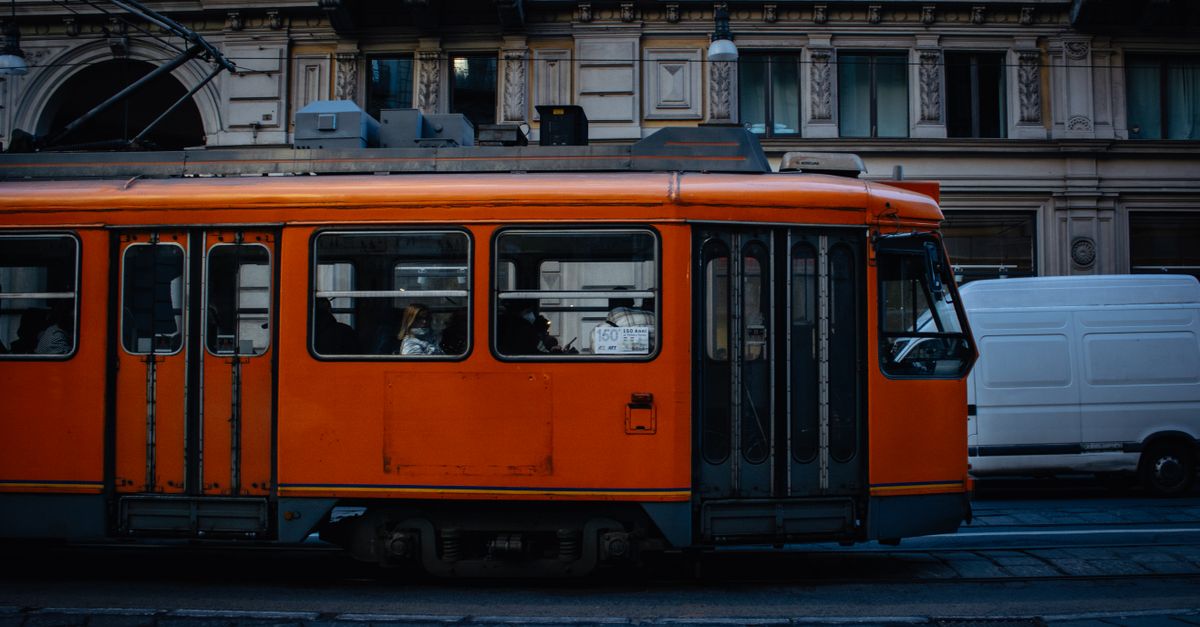 A striking orange tram travels through a bustling city street, showcasing urban public transportation.