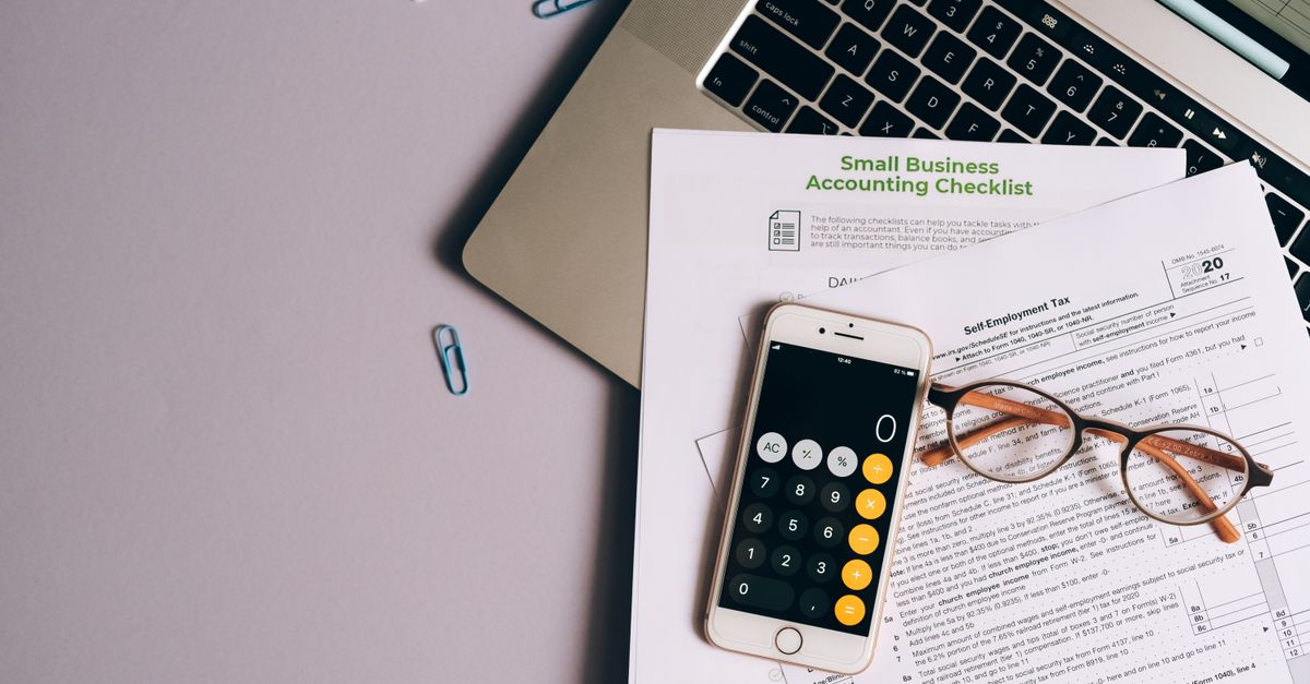 Flat lay of small business accounting tools including tax form, phone, and glasses on a desk.