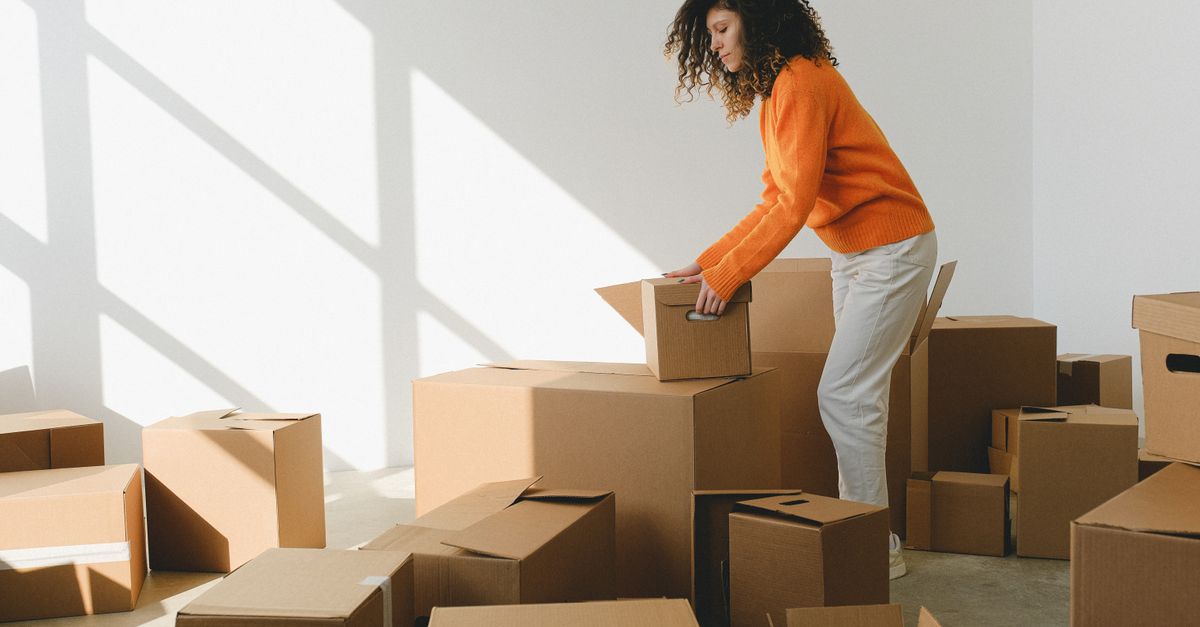 Side view of concentrated young lady with curly hair in casual clothes packing and arranging cardboard boxes while preparing for moving into new apartment in daylight