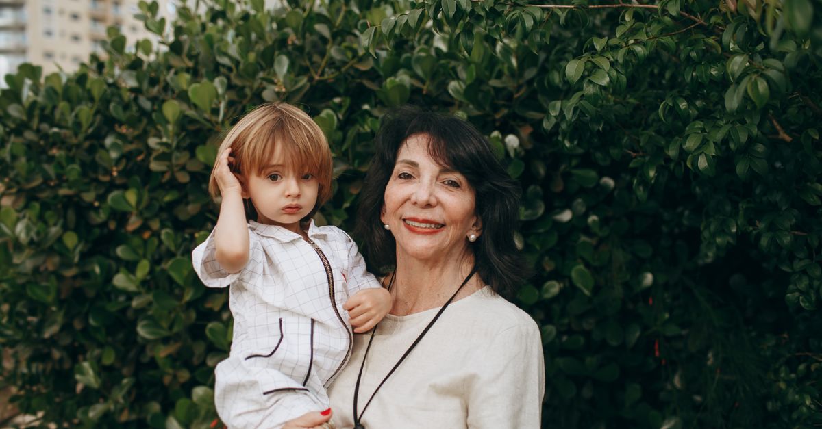 A loving grandmother with her grandchild smiling outdoors in a lush garden setting.