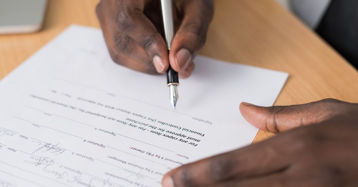 Close-up of a man's hands signing a formal document indoors.