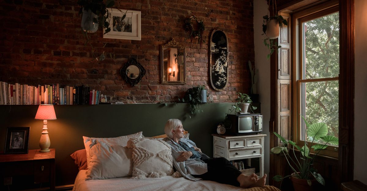 A senior woman relaxing in a cozy bedroom with vintage decor and natural light.