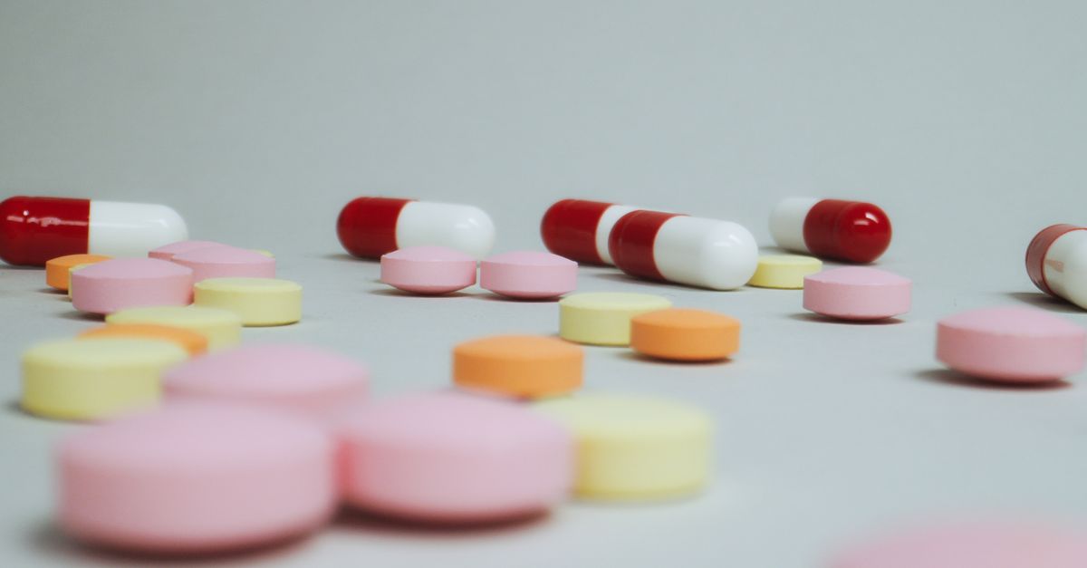Close-up of varied pills and capsules scattered on a white surface.